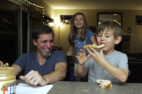 father daughter and son laughing over a peanut butter and jelly sandwhich