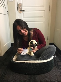 Christina Miranda showing a fabulous and unexpected tourism guest service example while she sits in a dog bed holding the toy dog delivered to her room at the Rodd Miramichi River Hotel.