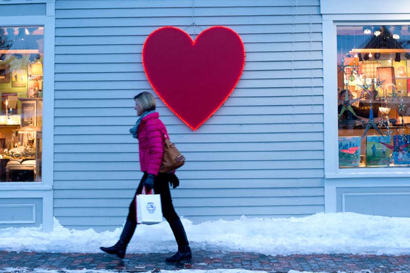 woman in red coat walking in front of building with red heart on wall