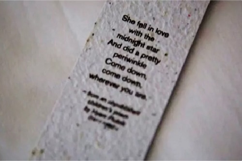 A white colored bookmark (embedded with flower seeds) with a poem written in black sits on a white background, showing that hotel amenities can have marketing value.