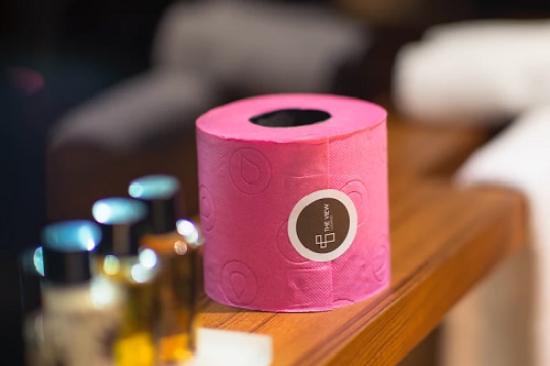 A roll of pink toilet paper sitting on a wood ledge that shows hotel amenities can have marketing value.