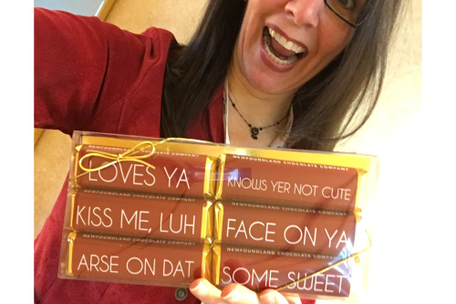 Chris Miranda holds up a collection of chocolate bars from the Newfoundland Chocolate Company. The six bars are in brown packaging with white typeface, and feature a variety of sayings. This is an excellent example of how to inspire word-of-mouth in tourism marketing.