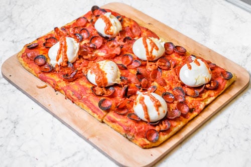 A rectangular pizza with red sauce and lots of pepperoni, plus six burrata cheeses sitting atop the pie, all resting on a wooden cutting board. Courtesy of Unregular Pizza as part of their ambitious marketing program that features bartering for pizza.